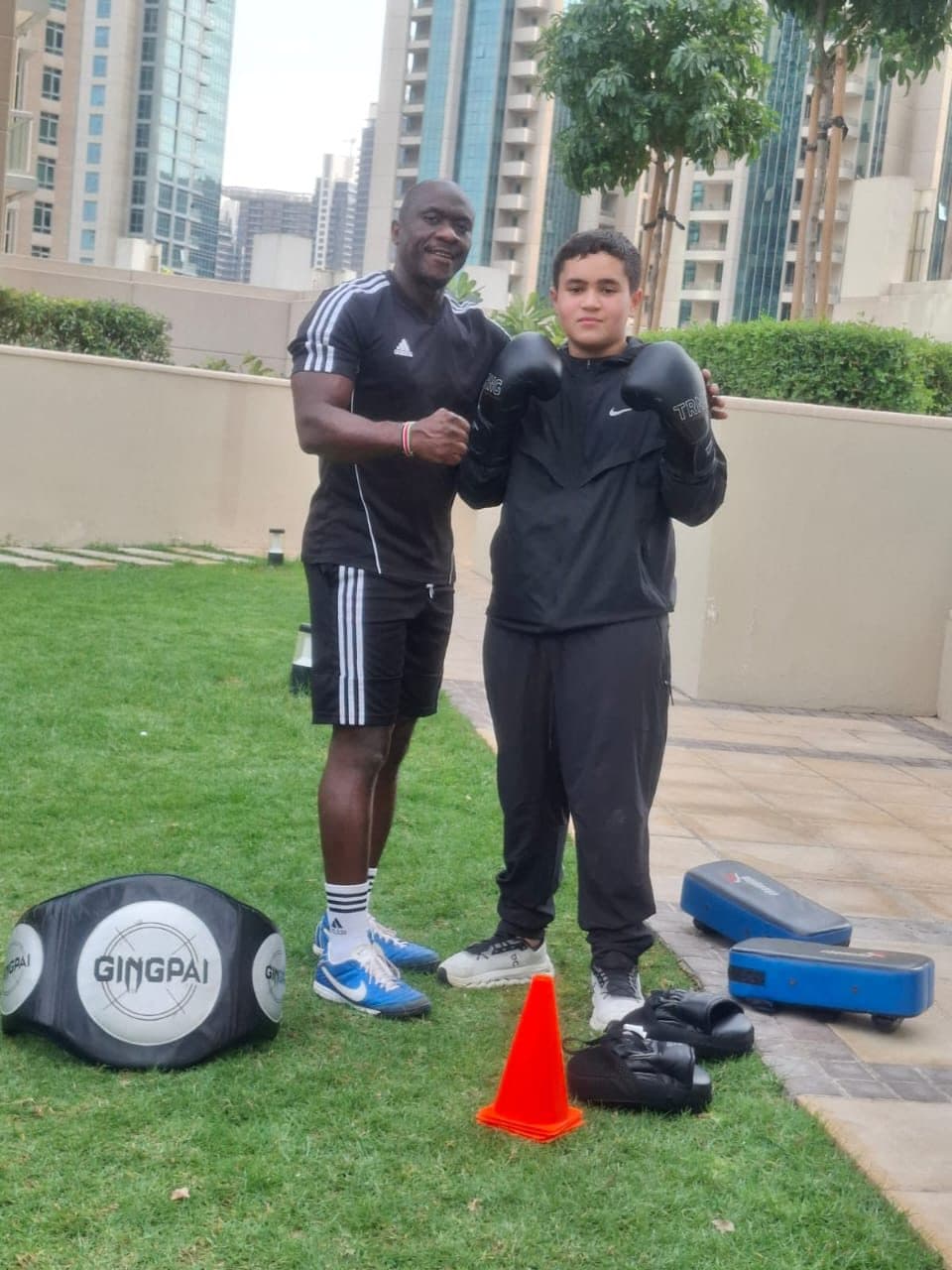 Two people setting up in a boxing guard on grass with pads and gloves nearby