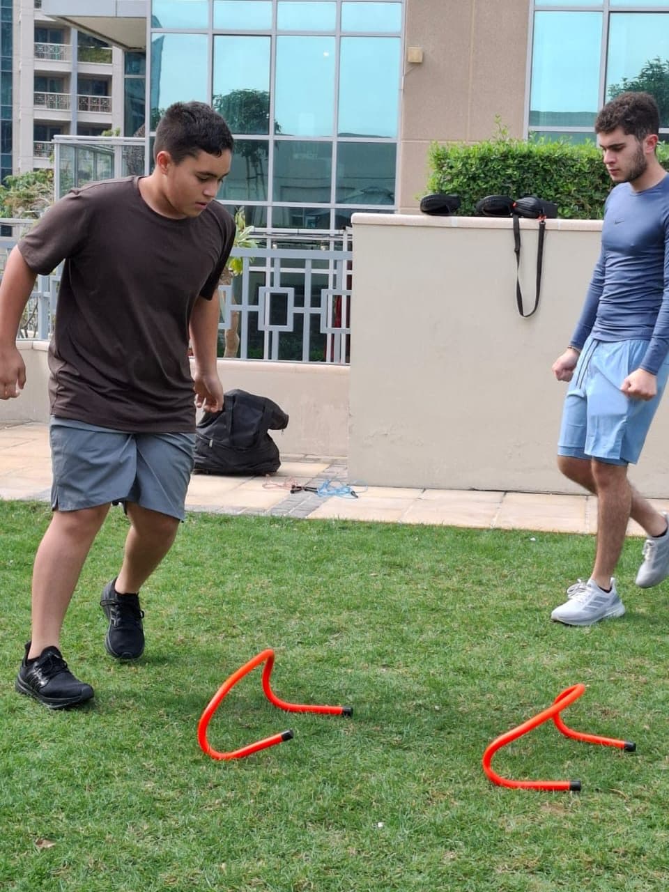 Two people working through an agility drill over hurdles on grass