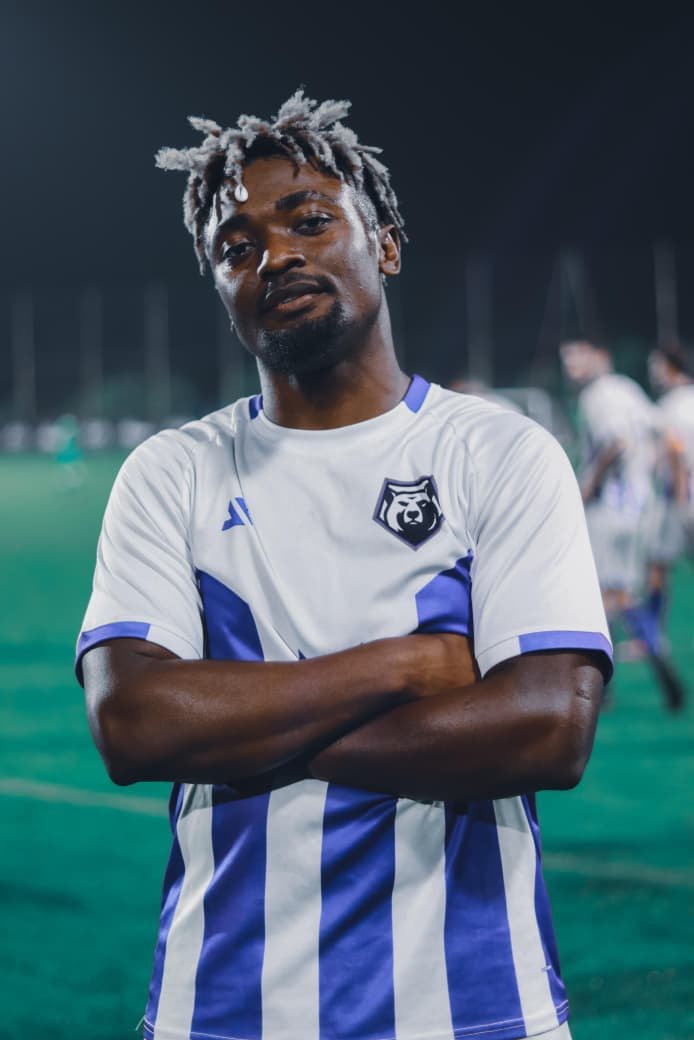 Footballer in a striped kit standing on the pitch with arms folded