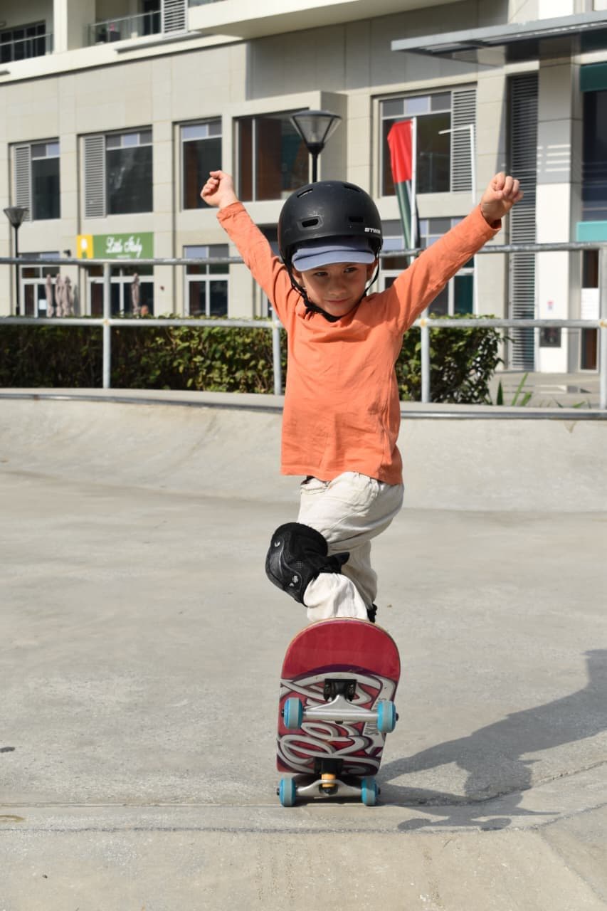 Young skateboarder celebrating with both arms raised on a skate plaza