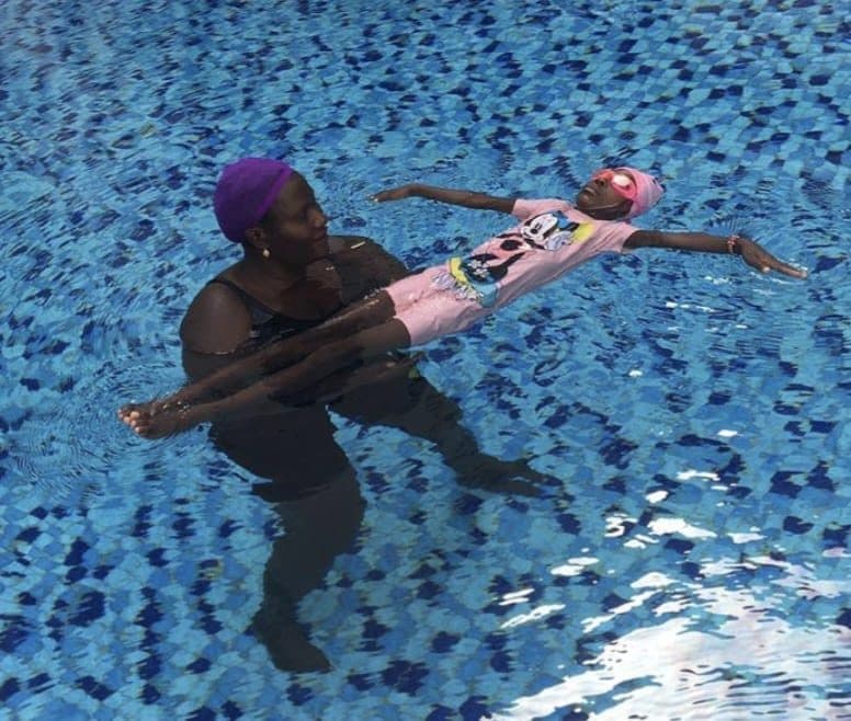 An adult supporting a child floating on their back in a pool